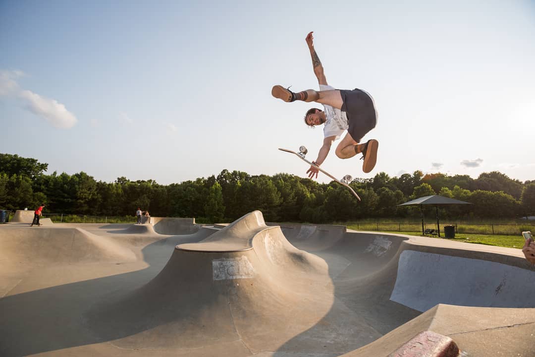 man soaring above the skatepark flipping his skateboard under him